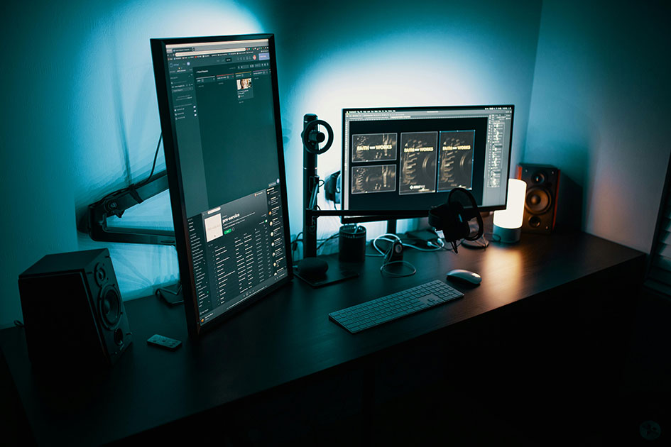 About-Us_Right_Image Photograph showing desk with keyboard, mouse and two monitors on stands, one monitor is portrait the other landscape. Moodlighting in blue to set the scene.