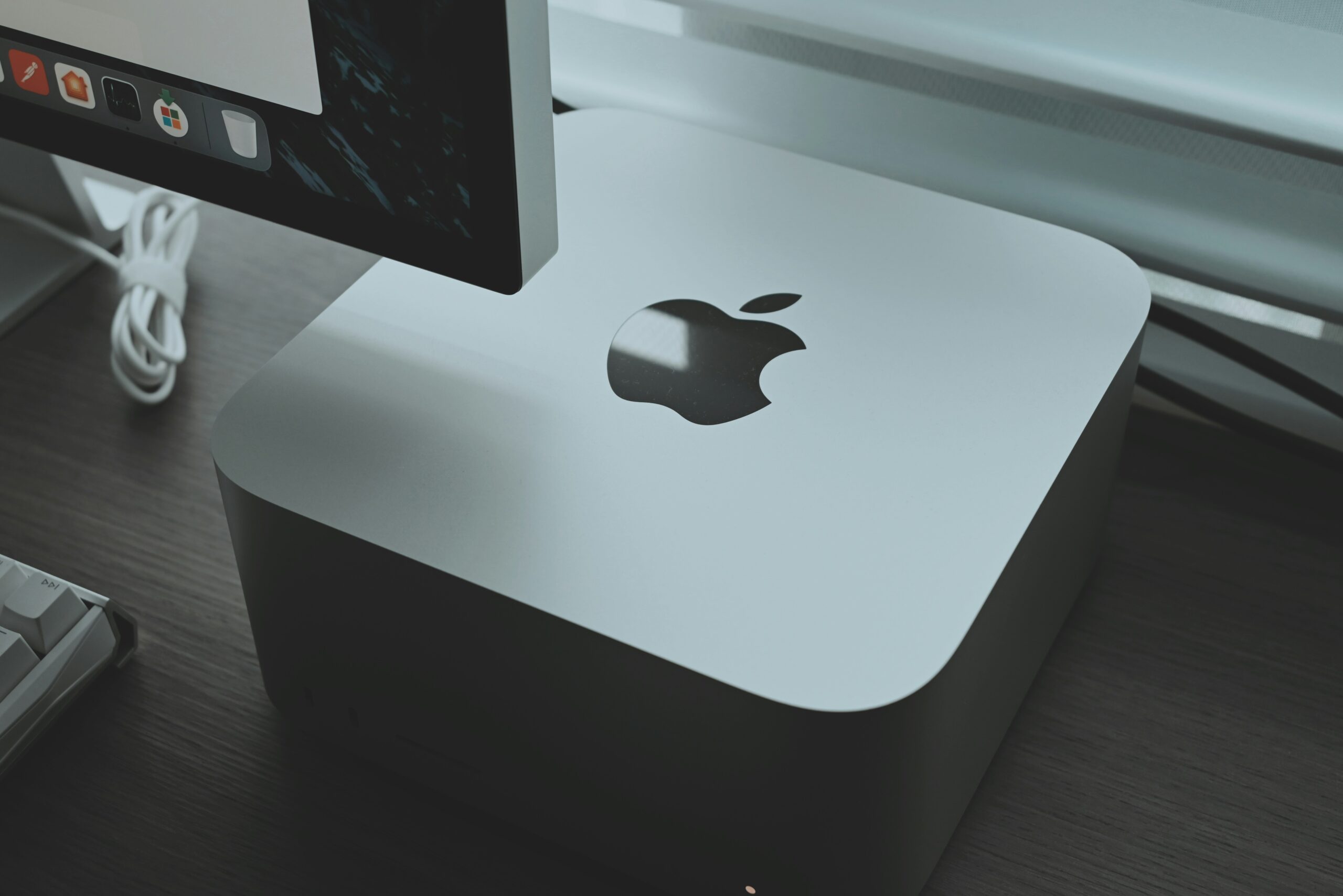 Apple_Mac_Mini_Remote_Support Photograph of and Apple Mac Mini on a desk with the corner of an Apple Mac Monitor and keyboard to the left of it.