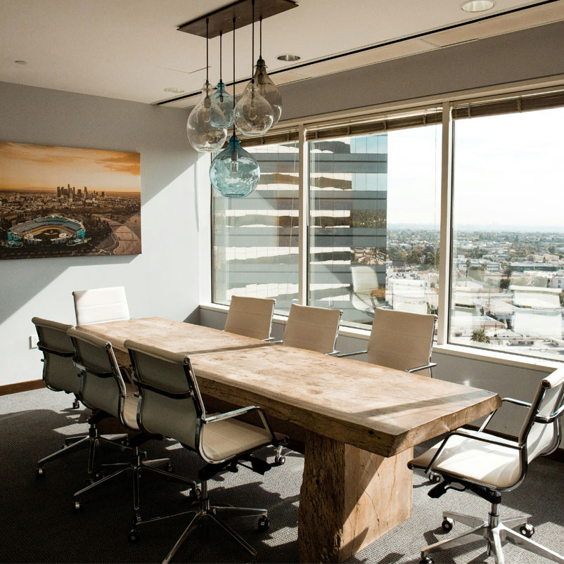 Meeting_Room_01 Photograph of modern office meeting room with pannelled glass overlooking city. The table is solid rustic wood surrounded by eight modern leather chairs with stainless steel frames and spoked feet with wheels. Modern blue glass and smoked glass shades hang above the table.