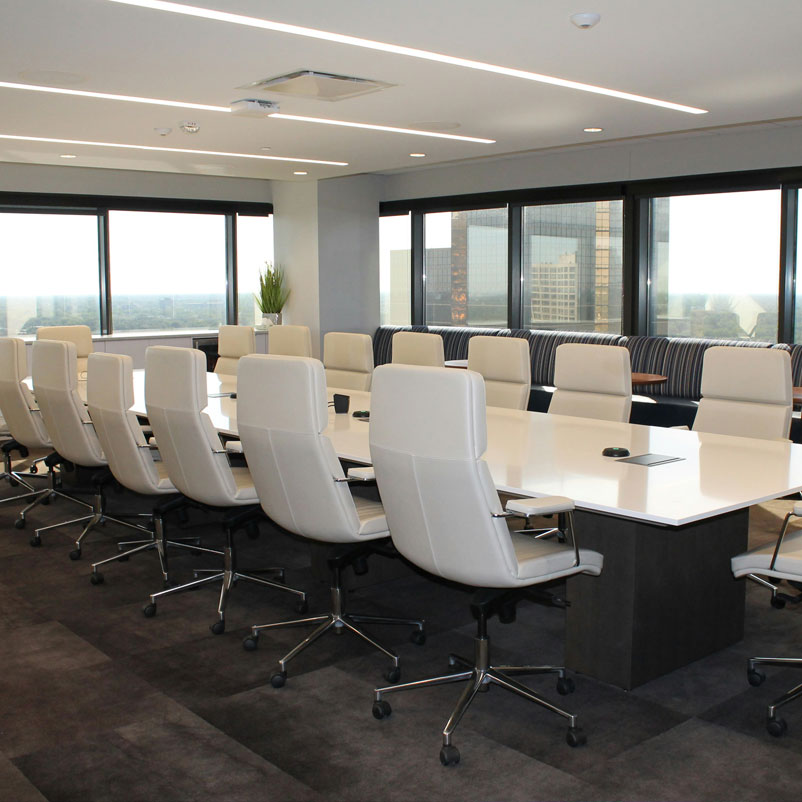 Meeting_Rooms Photograph of modern board room with panoramic view of city behind. Long white table with sixteen white leather armed chairs on five stainless steel legs with wheels on the bottom.