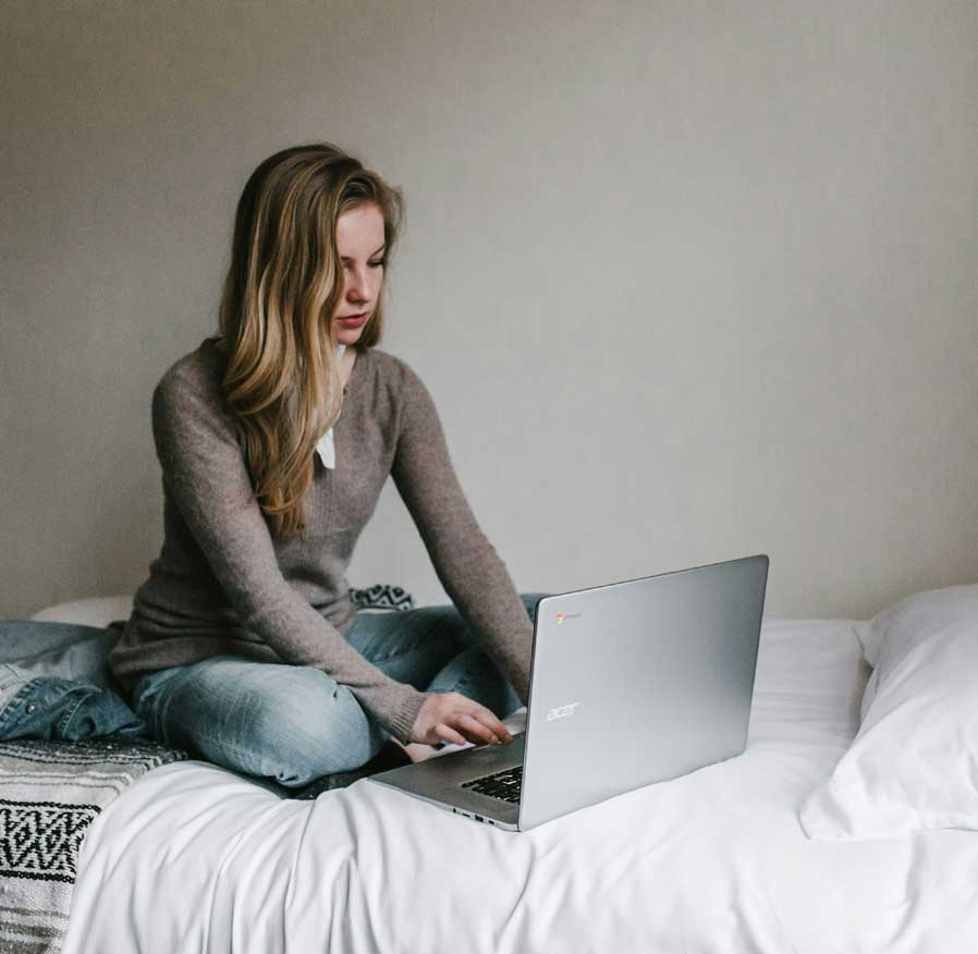 Woman seated on bed at home using laptop