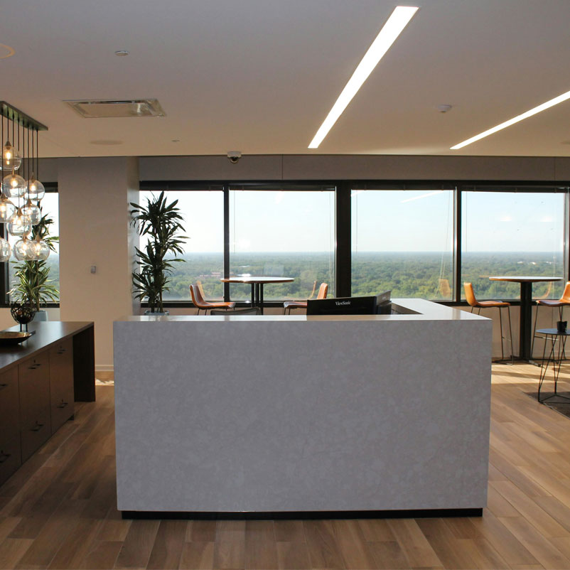 Reception_01 Photograph of open plan reception room with tall round desks and stools placed at windows and an L shaped desk just showing the top of two monitors at angles in the corner.